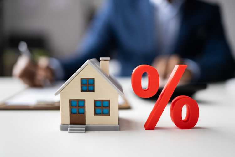 percentage sign next to a model home, in the background man signing on a mortgage